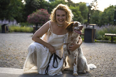 Junge Frau hockt mit Hund im Park - YBF00065