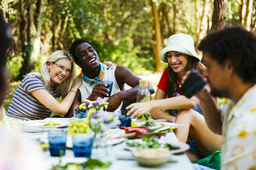 Happy friends enjoying picnic lunch in garden - EBSF03731