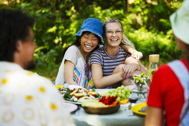 Cheerful friends enjoying food at picnic table in garden - EBSF03734