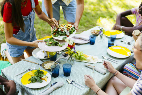 Friends serving food at picnic table in garden - EBSF03735