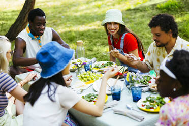 Lächelnde Freunde, die sich am Picknicktisch im Garten unterhalten - EBSF03737
