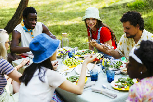 Smiling friends having conversation at picnic table in garden - EBSF03737