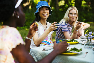 Lächelnde Freunde beim Mittagessen am Picknicktisch im Garten - EBSF03738