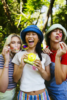 Smiling friends blowing bubbles in garden - EBSF03754