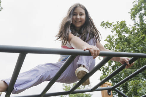 Lächelndes Mädchen sitzt auf dem Klettergerüst auf dem Spielplatz - OSF01936