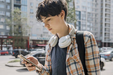 Teenage boy using smart phone and walking in city - ANAF01896