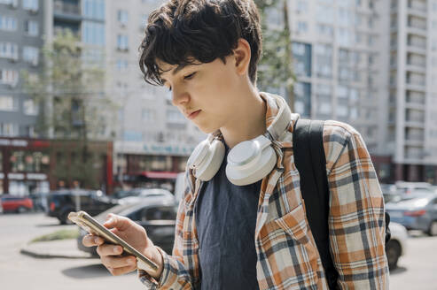 Teenage boy using smart phone and walking in city - ANAF01896