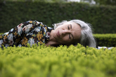 Ältere Frau liegt auf Pflanzen im Park - FLLF00898