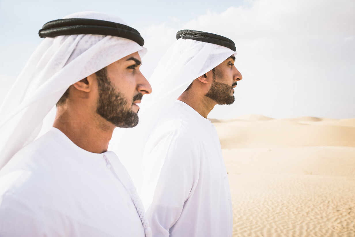 Arabian men witk kandora walking in the desert - Portrait of two middle  eastern adults with traditional arabic dress stock photo