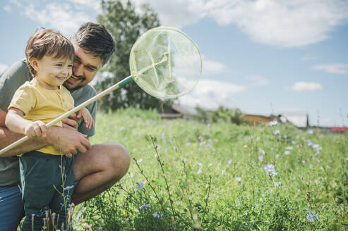 Glücklicher Vater fängt Schmetterling mit Sohn im Garten - ANAF01909