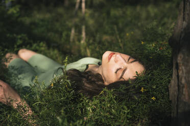 Frau mit geschlossenen Augen im Gras liegend im Wald - YBF00071