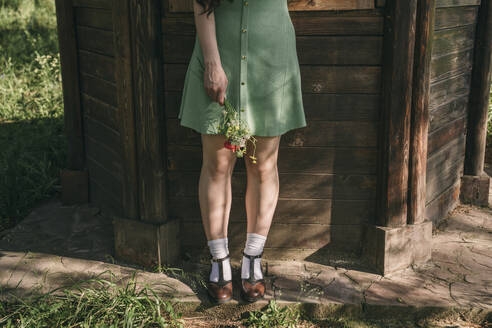 Frau mit Wildblumen vor einer Holzwand stehend - YBF00073
