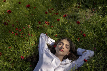 Woman relaxing on grass with poppy flowers - YBF00075