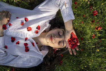 Smiling young woman relaxing on grass with poppy flowers - YBF00076