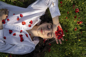 Lächelnde junge Frau, die sich im Gras mit Mohnblumen entspannt - YBF00076