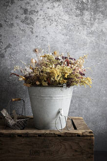 Arrangement aus getrockneten Blumen in einem Metalleimer, der auf einer Holzkiste steht - EVGF04352