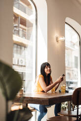 Glückliche Frau mit Smartphone in einem Café sitzend - JOSEF20402