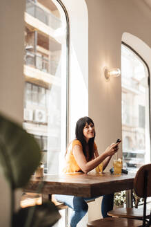 Happy woman with smart phone sitting in cafe - JOSEF20402