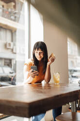 Smiling woman with credit card using smart phone in cafe - JOSEF20405