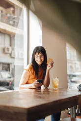 Happy woman sitting with credit card and smart phone in cafe - JOSEF20406