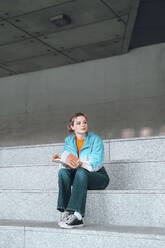 Nachdenkliches Mädchen mit Buch auf der Treppe sitzend - YHF00047