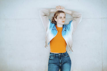 Woman with hands on head standing in front of wall - YHF00060