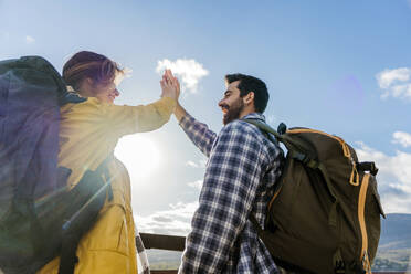 Happy couple giving high-five under sky on sunny day - JJF00971