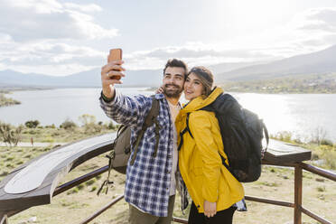 Smiling tourist taking selfie through smart phone standing at observation point - JJF00980