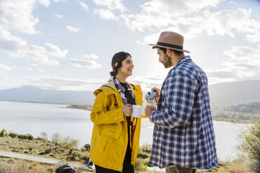 Glückliche Frau sieht Mann an, der Kaffee vor einem See serviert - JJF00999