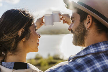 Couple toasting coffee mugs on sunny day - JJF01012