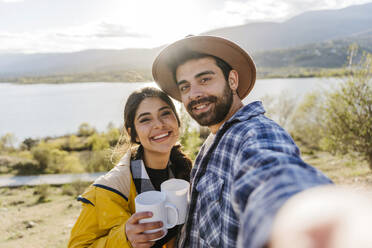 Smiling man taking selfie with girlfriend holding coffee mug - JJF01013