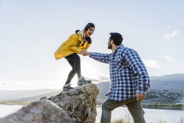 Mann hält die Hände einer auf einem Felsen stehenden Frau - JJF01024