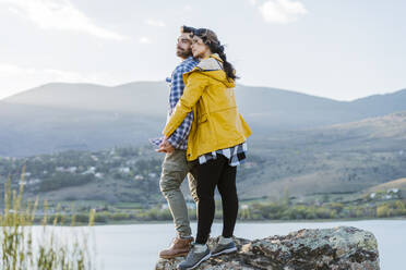 Couple holding hands standing on rock in front of mountain - JJF01031