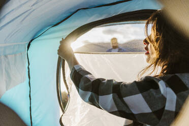 Young woman unzipping tent on vacation - JJF01047