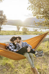 Boyfriend and girlfriend spending leisure time sitting in hammock - JJF01054