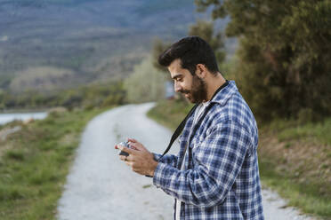 Smiling man using drone controller on footpath - JJF01066