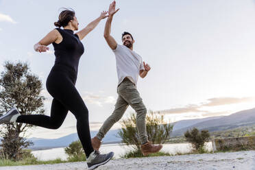 Couple giving high-five and running on footpath - JJF01077