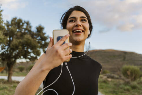 Happy woman listening music and running on footpath - JJF01078