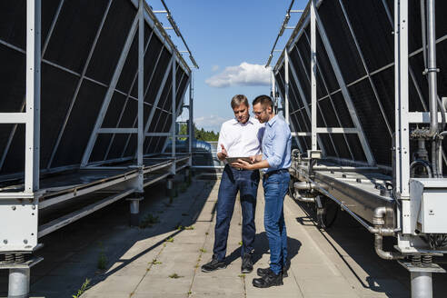 Zwei Führungskräfte nutzen ein digitales Tablet, während sie auf einem Dach neben einer Kühlanlage stehen - DIGF20151