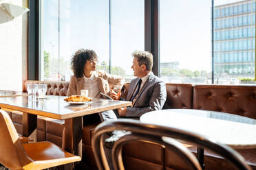 Senior businessman and beautiful hispanic businesswoman meeting in a bar restaurant - Two colleagues bonding in a cafe after work - DMDF00588