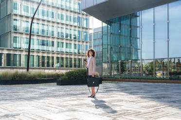 Beautiful hispanic businesswoman with elegant suit walking in the business centre- Adult female with business suit and holding mobile phone portrait outdoors - DMDF00590