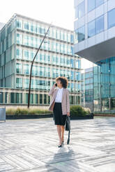 Beautiful hispanic businesswoman with elegant suit walking in the business centre- Adult female with business suit and holding mobile phone portrait outdoors - DMDF00592