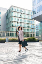 Beautiful hispanic businesswoman with elegant suit walking in the business centre- Adult female with business suit and holding mobile phone portrait outdoors - DMDF00594