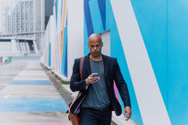 Young business man going to work in the morning passing by an urban area of the city with colored walls.Representation of a successful sales person reaching the top of the career. - DMDF00725