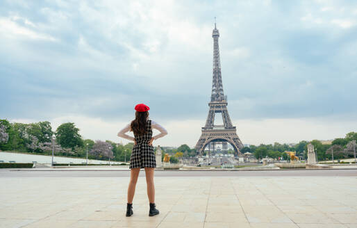 Schöne junge Frau, die Paris und den Eiffelturm besucht. Pariser Mädchen mit rotem Hut und modischer Kleidung, die sich im Stadtzentrum und im Bereich der Sehenswürdigkeiten amüsiert - DMDF00873