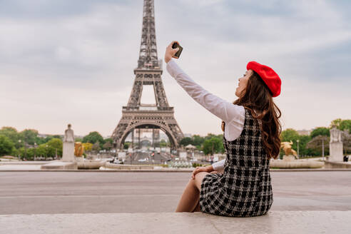 Schöne junge Frau, die Paris und den Eiffelturm besucht. Pariser Mädchen mit rotem Hut und modischer Kleidung, die sich im Stadtzentrum und im Bereich der Sehenswürdigkeiten amüsiert - DMDF00874