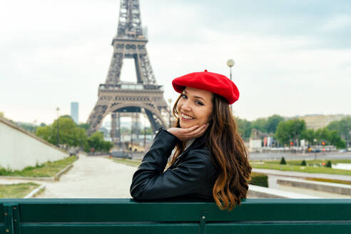 Schöne junge Frau, die Paris und den Eiffelturm besucht. Pariser Mädchen mit rotem Hut und modischer Kleidung, die sich im Stadtzentrum und im Bereich der Sehenswürdigkeiten amüsiert - DMDF00877