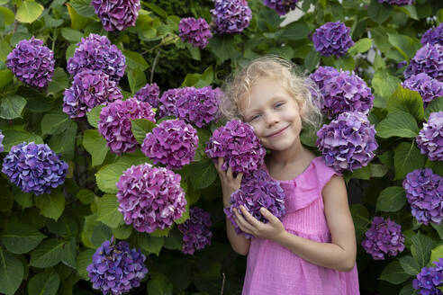 Lächelndes Mädchen steht vor Hortensienblüten im Garten - SVKF01572