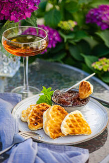 High angle of appetizing sweet waffles served with peach jam on round table near glass with drink in garden with blooming purple Hydrangea flowers - ADSF46233