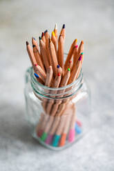Collection of colorful pencils stacked in glass jar placed on table against gray background - ADSF46234